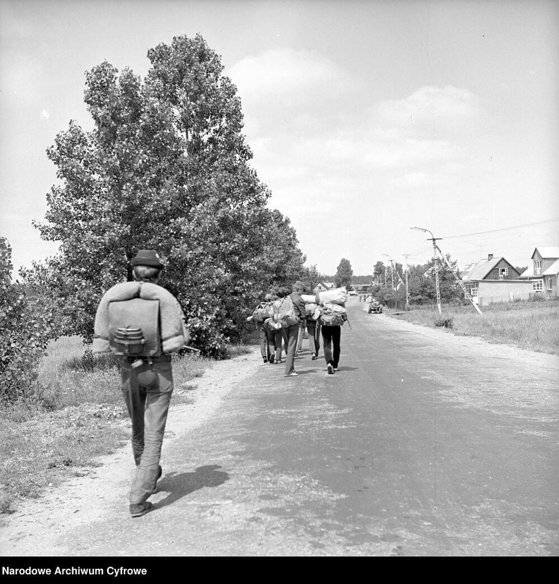 Zdjęcie ilustracyjne/Wakacje na Suwalszczyźnie 1972 rok. Turyści z plecakami maszerują wiejską drogą. W tle zabudowa wsi
